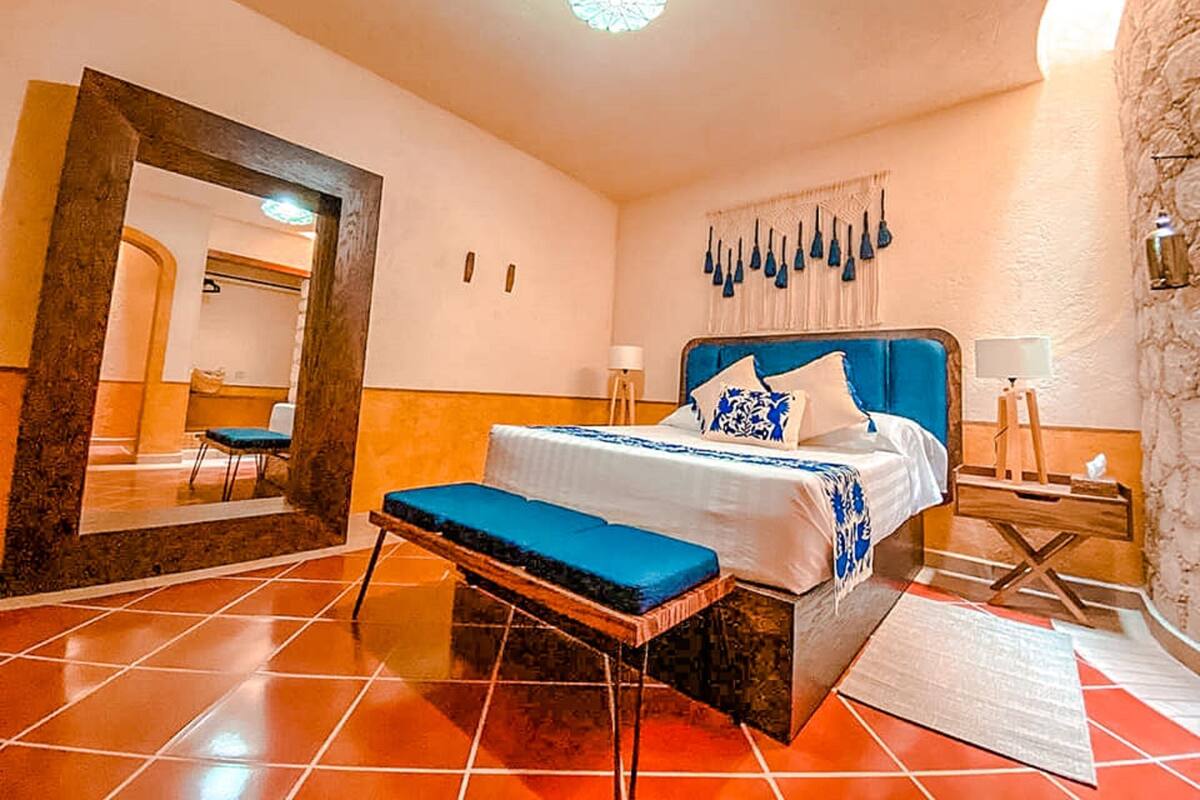 Een hotelkamer met een bed, een bankje, een spiegel, een wandlamp en een plafondlamp.
