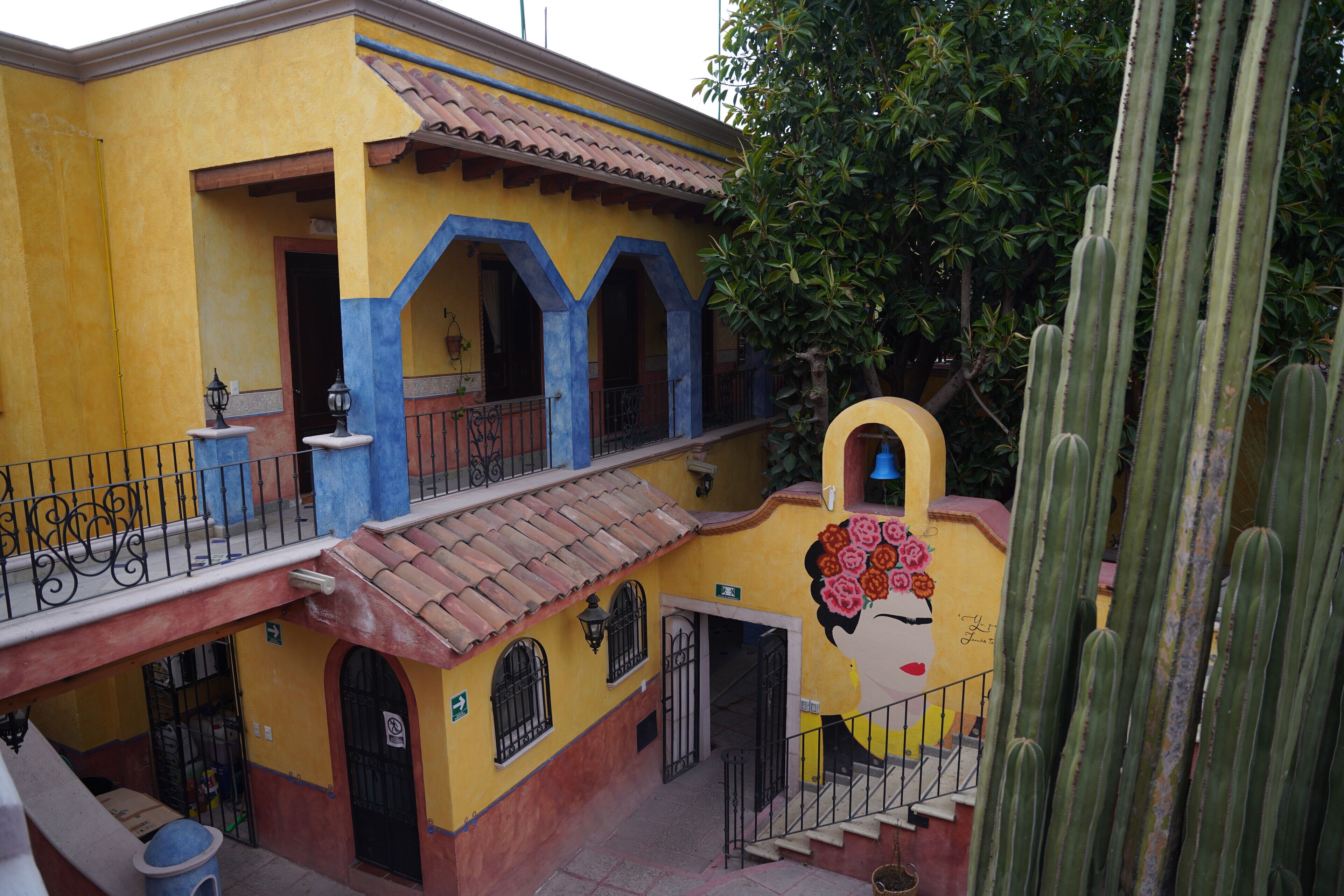 A building with a yellow facade, blue arches, and a staircase leading to a balcony.