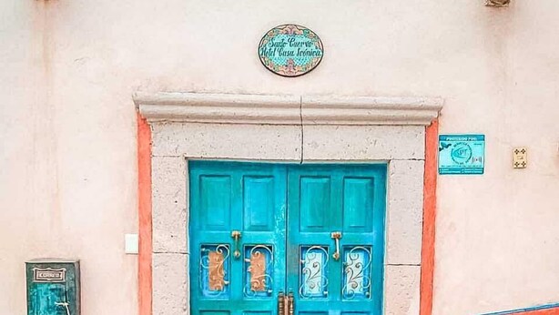 A turquoise double door with decorative glass panels, a sign above indicating a hotel, and stone steps leading up to the entrance. - Hotel Boutique Santo Cuervo (Ezequiel Montes)