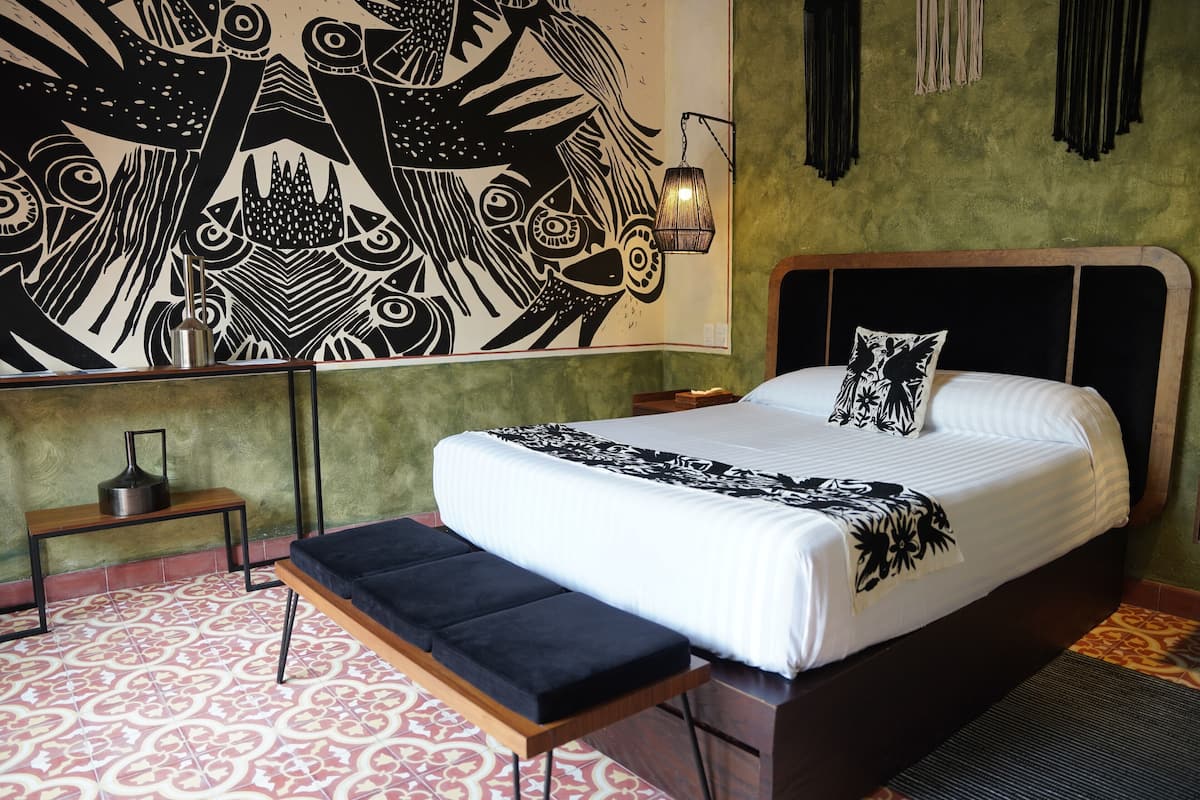 Een kamer met een bed, een bankje, een wanddecoratie en een hanglamp.