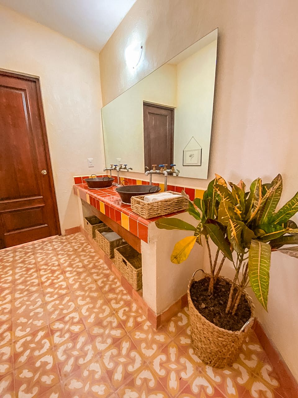 A bathroom with a tiled floor, a sink with a mirror above, and a potted plant.