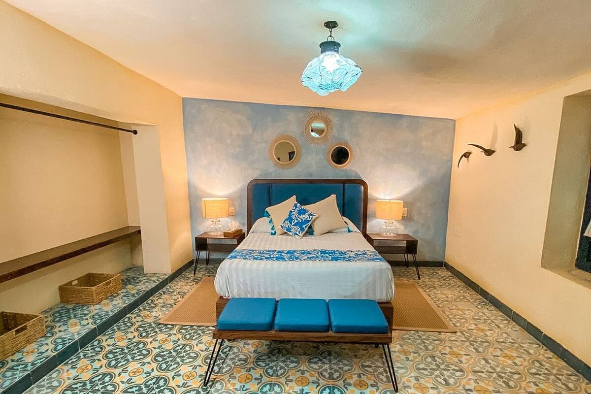 Een slaapkamer met een bed, twee nachtkastjes, een hanglamp, een spiegel aan de muur en een vloer met een patroon.
