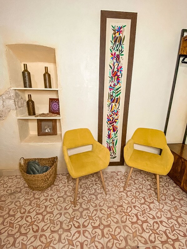 Una habitación con baldosas de diseño, dos sillas amarillas, una estantería con objetos decorativos y una obra de arte vertical.