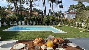 Una mesa de madera con platos, vasos, croissants, una jarra de jugo de naranja y frascos de mermelada.