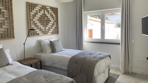 Un dormitorio con dos camas, un ventanal con cortinas, una lámpara de techo y un televisor montado en la pared.