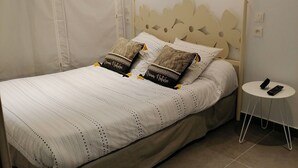 A neatly made bed with a striped white and beige duvet, two pillows with a nature-themed design, and a small bedside table with a remote control. - Ideal apartment for three people (Cerbère)