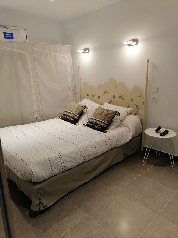 A neatly made bed with a striped white and beige duvet, two pillows with a nature-themed design, and a small bedside table with a remote control.