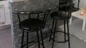 A kitchen with a granite countertop, two black bar stools, a white dining table with a candle, and a wall-mounted TV. - Ideal apartment for three people (Cerbère)