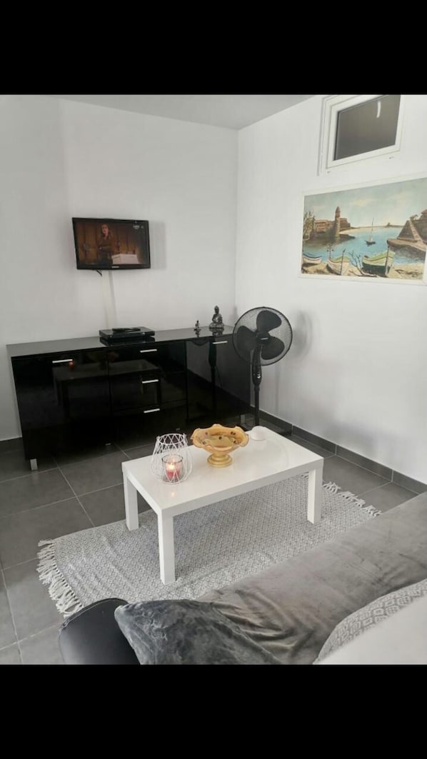 Una sala de estar moderna con un sofá blanco, una mesa de centro con objetos decorativos, un mueble de entretenimiento negro y un televisor montado en la pared.