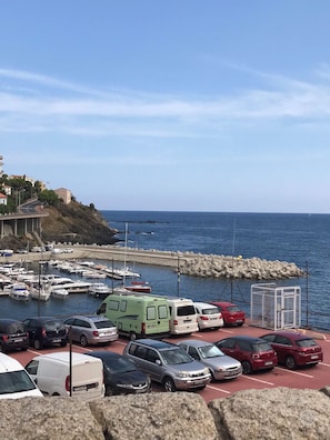 Una marina con coches estacionados y barcos, una costa rocosa y una vista despejada del mar.