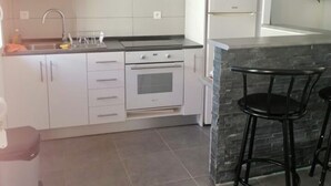 A modern kitchen with white cabinets, a stainless steel range hood, a built-in oven, a refrigerator, and a small island with bar stools. - Ideal apartment for three people (Cerbère)