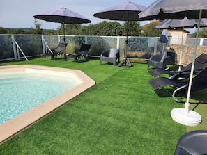 Une piscine bordée de gazon synthétique, avec des chaises longues et des parasols.