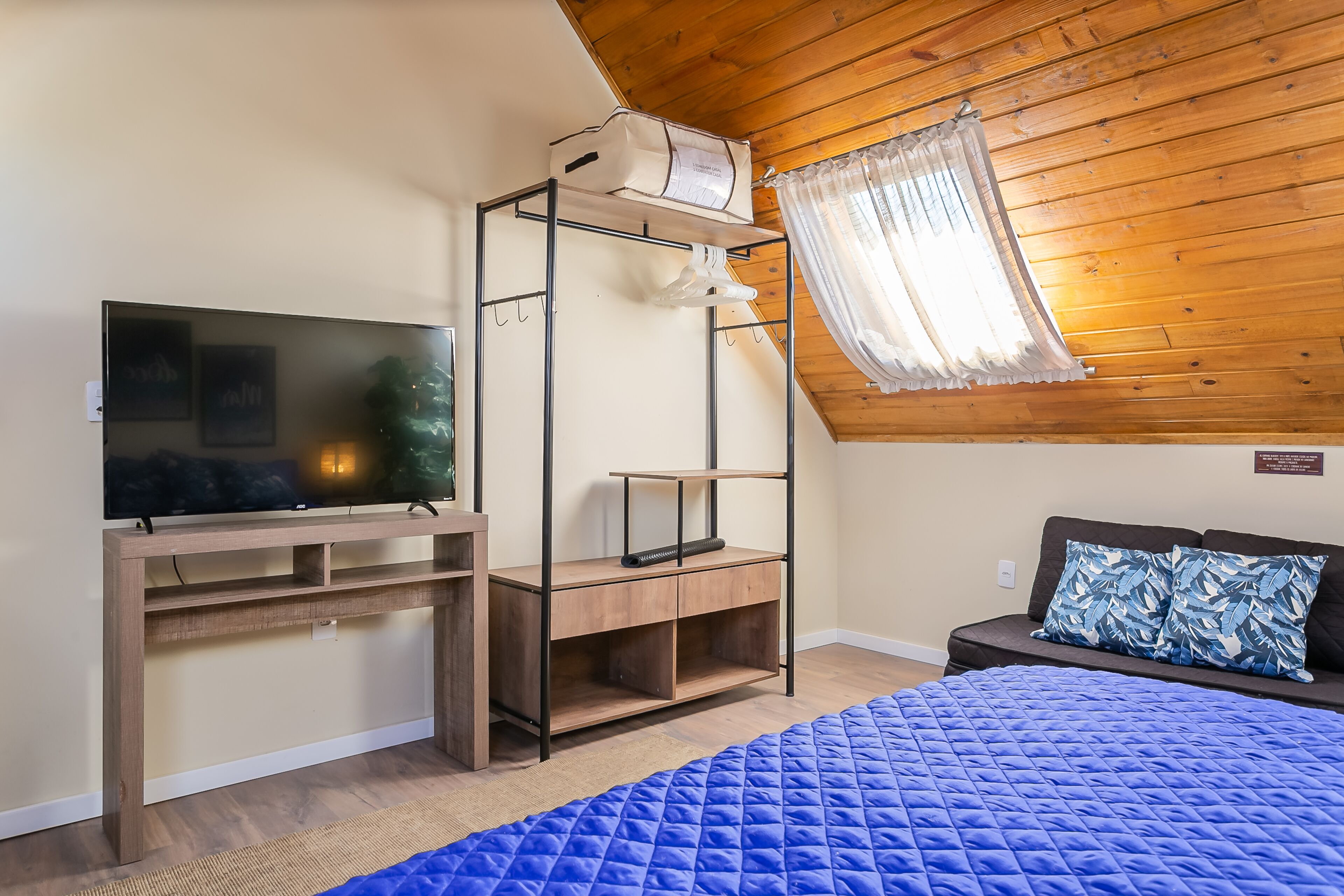 A bedroom with a bed, a TV, a wooden desk, a shelf, and a ceiling fan.