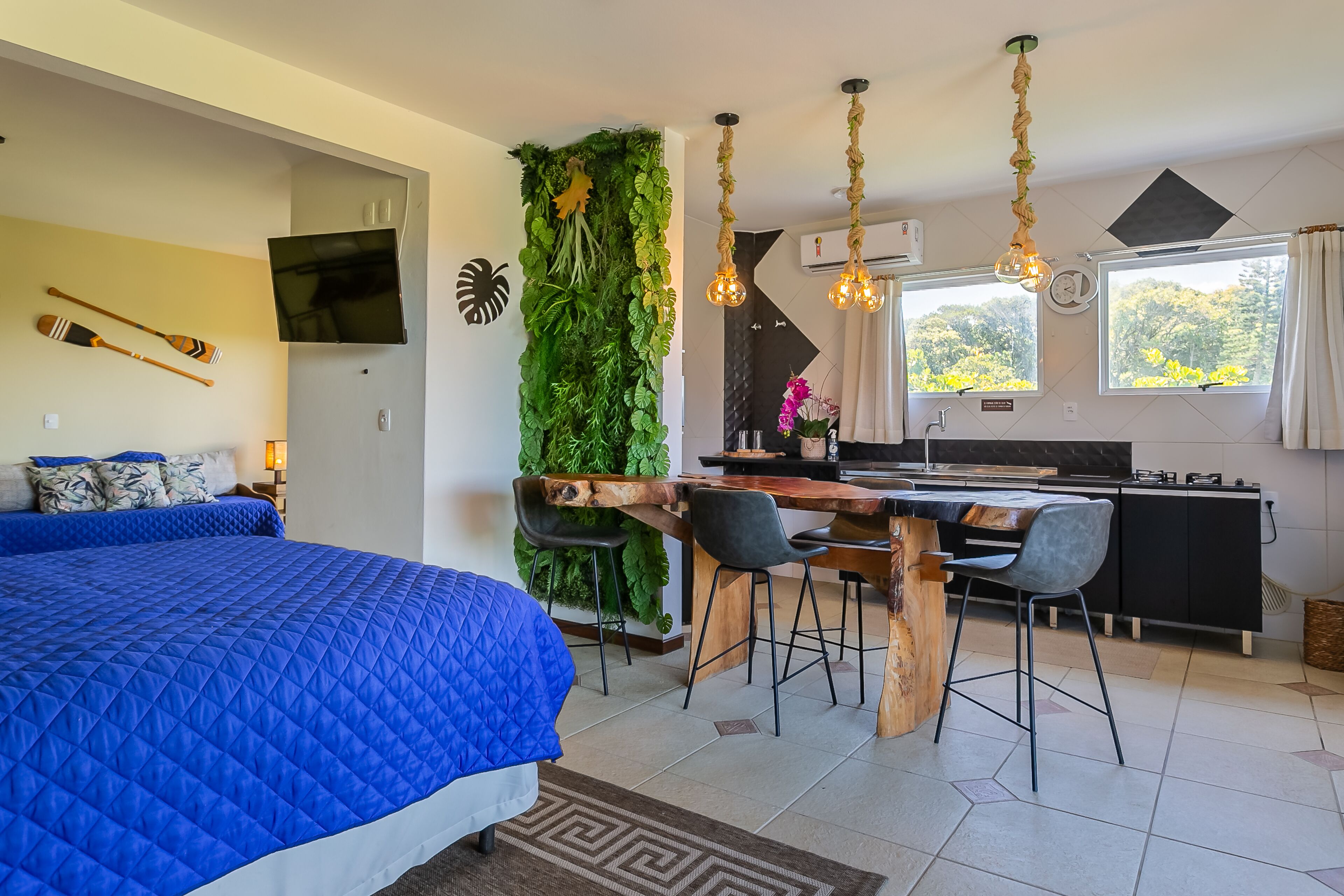 Una moderna camera d'albergo con un letto grande, un'area pranzo con tavolo e sedie in legno, una cucina con piano di lavoro nero e un soggiorno con televisore e decorazioni murali.