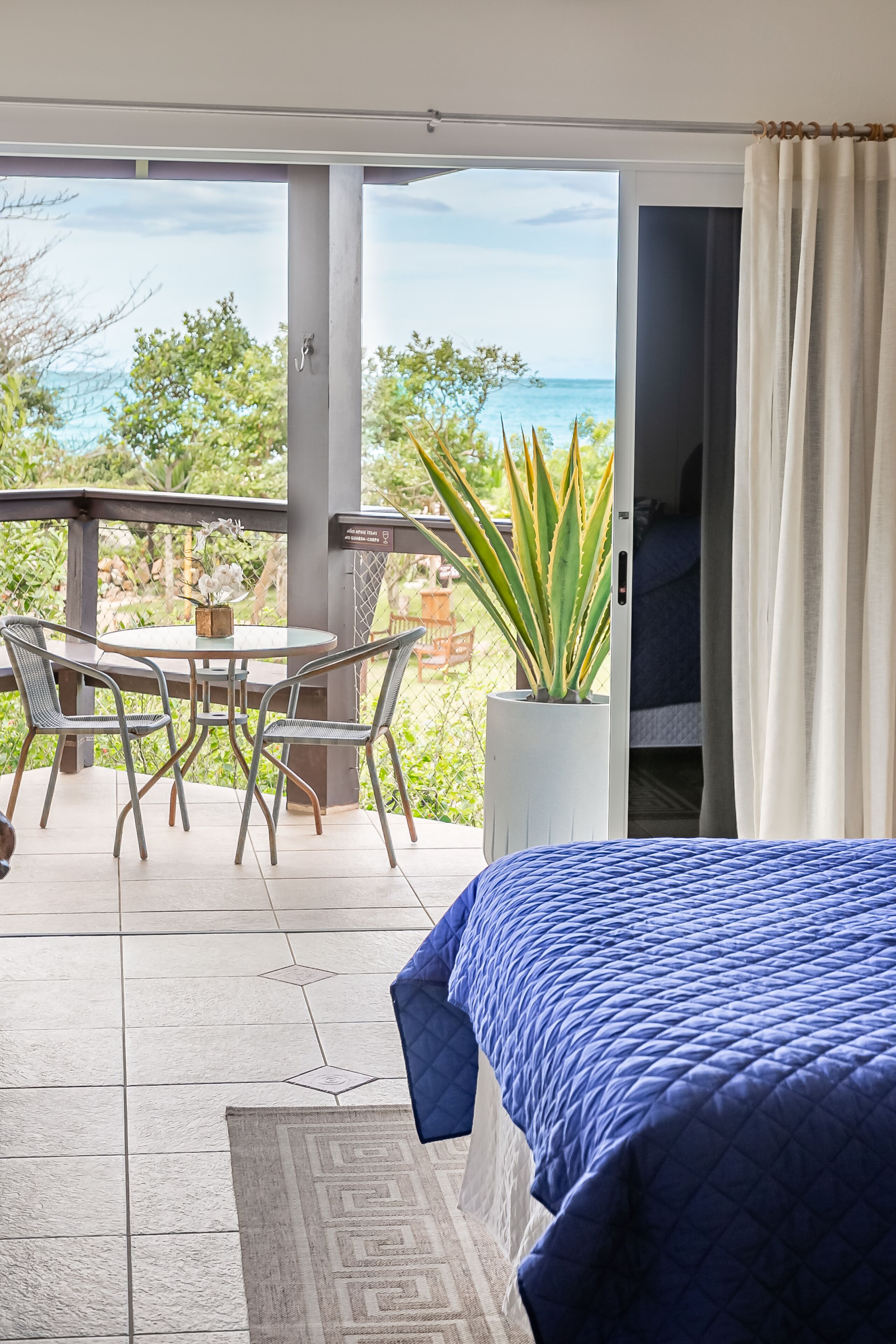 Een slaapkamer met een bed, een balkon met een tafel en stoelen, en uitzicht op zee.