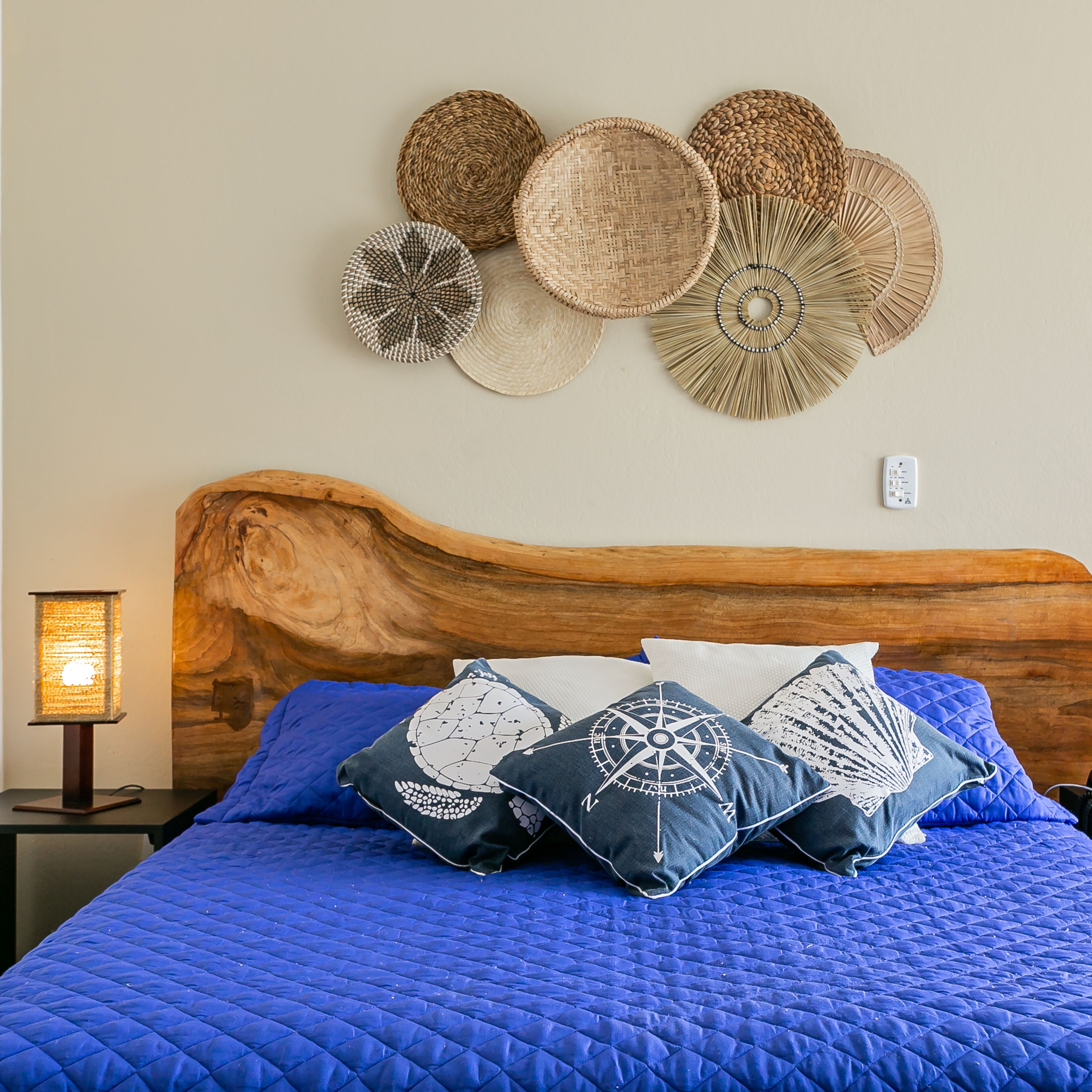A bed with a blue quilt, a wooden headboard, and decorative woven wall hangings.