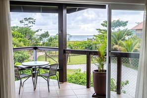 A balcony with a table and chairs, a potted plant, and a view of the sea and greenery. - Pénareia Floripa (Florianópolis)