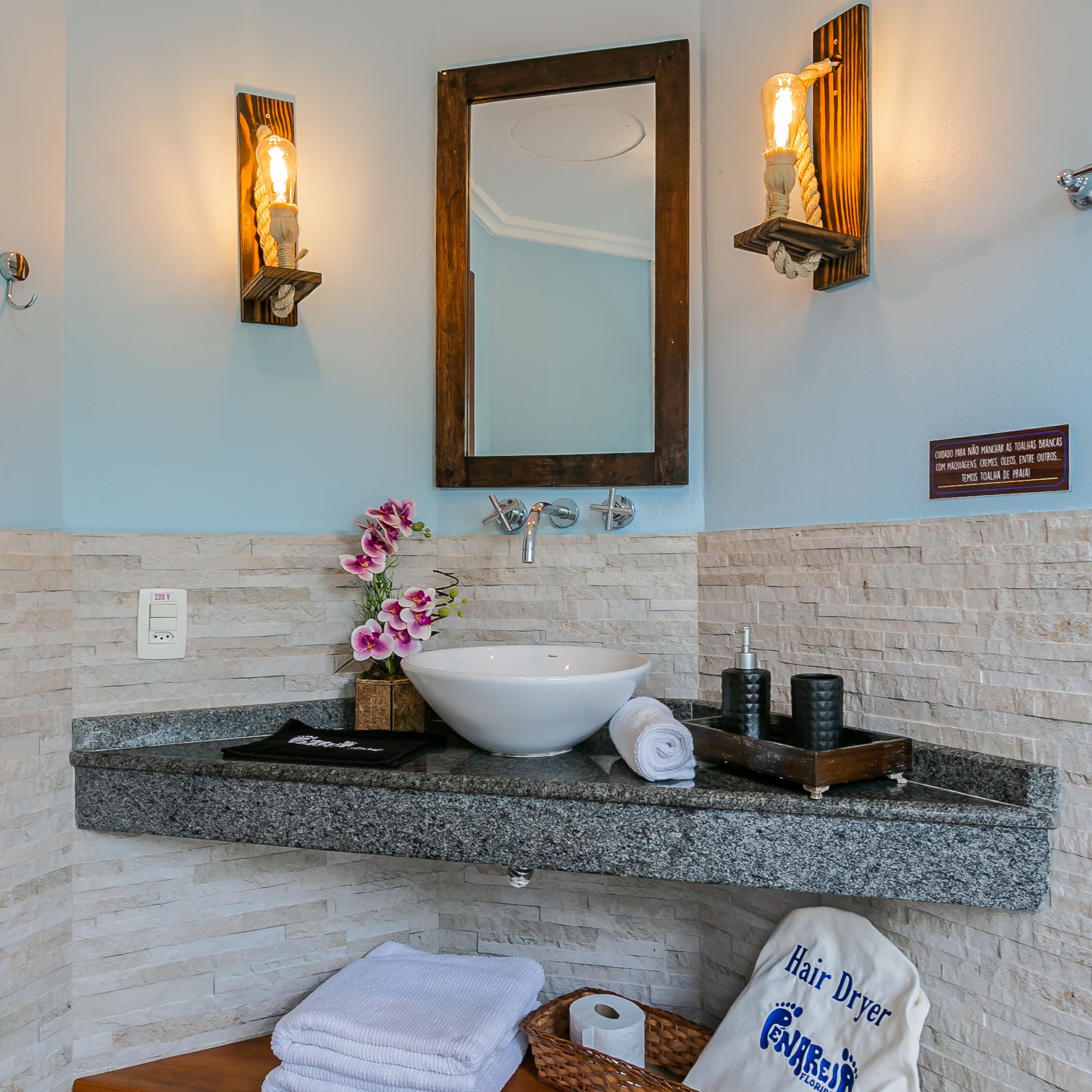 A bathroom with a white sink, a mirror, two wall-mounted lights, a towel, and a sign.