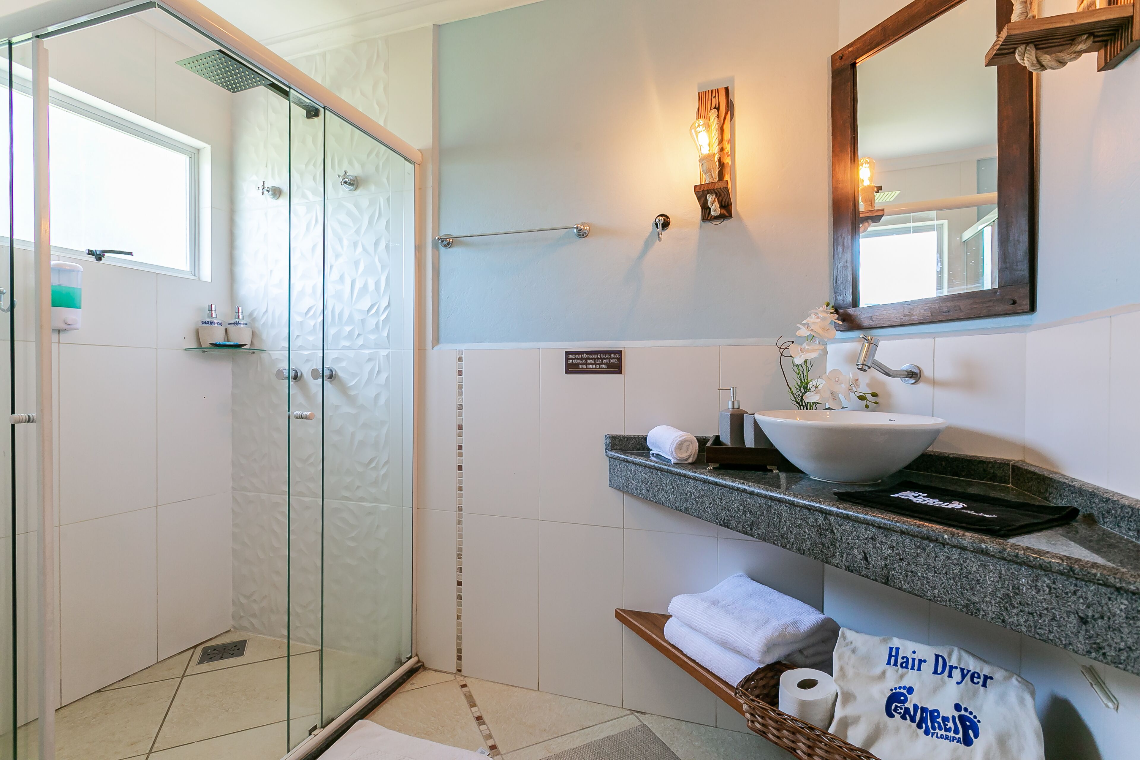 Un baño con cabina de ducha de vidrio, lavamanos con lavabo a la vista y toallero.