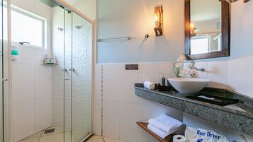 Un baño con cabina de ducha de vidrio, lavamanos con lavabo a la vista y toallero.