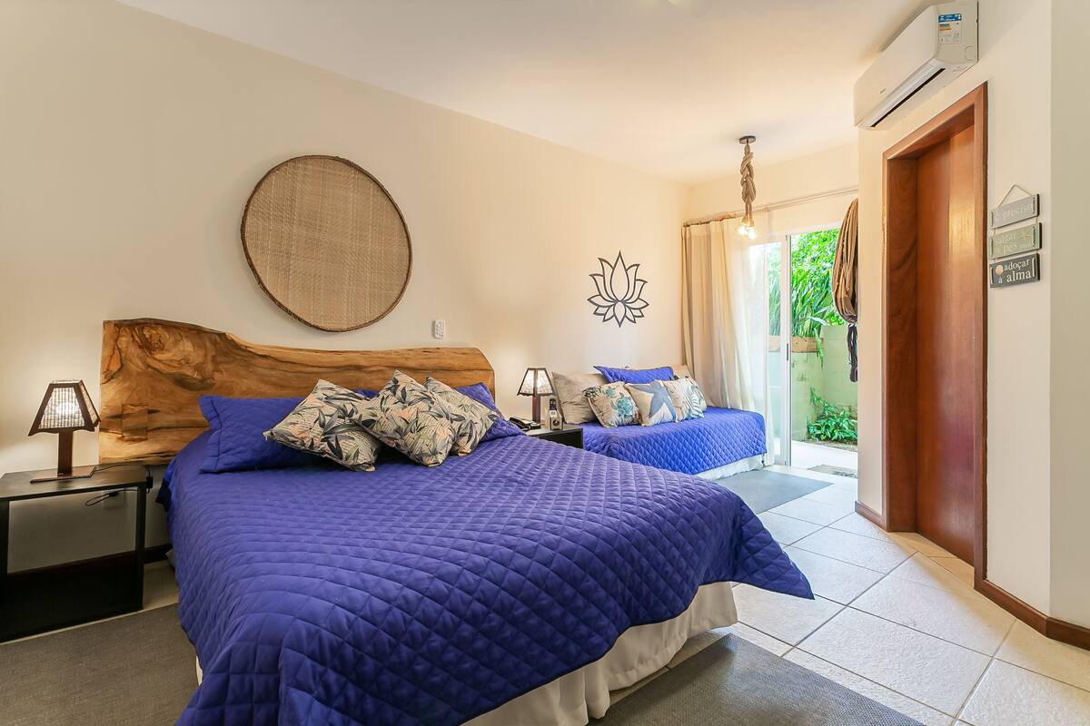 A bedroom with two beds, a wooden headboard, a wall-mounted round mirror, and a door leading to a balcony.