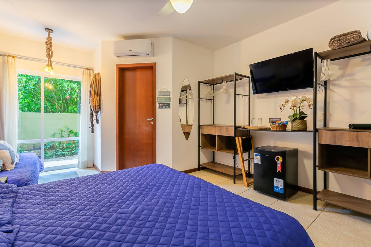 A bedroom with a large bed, a TV, a wardrobe, and a small refrigerator.