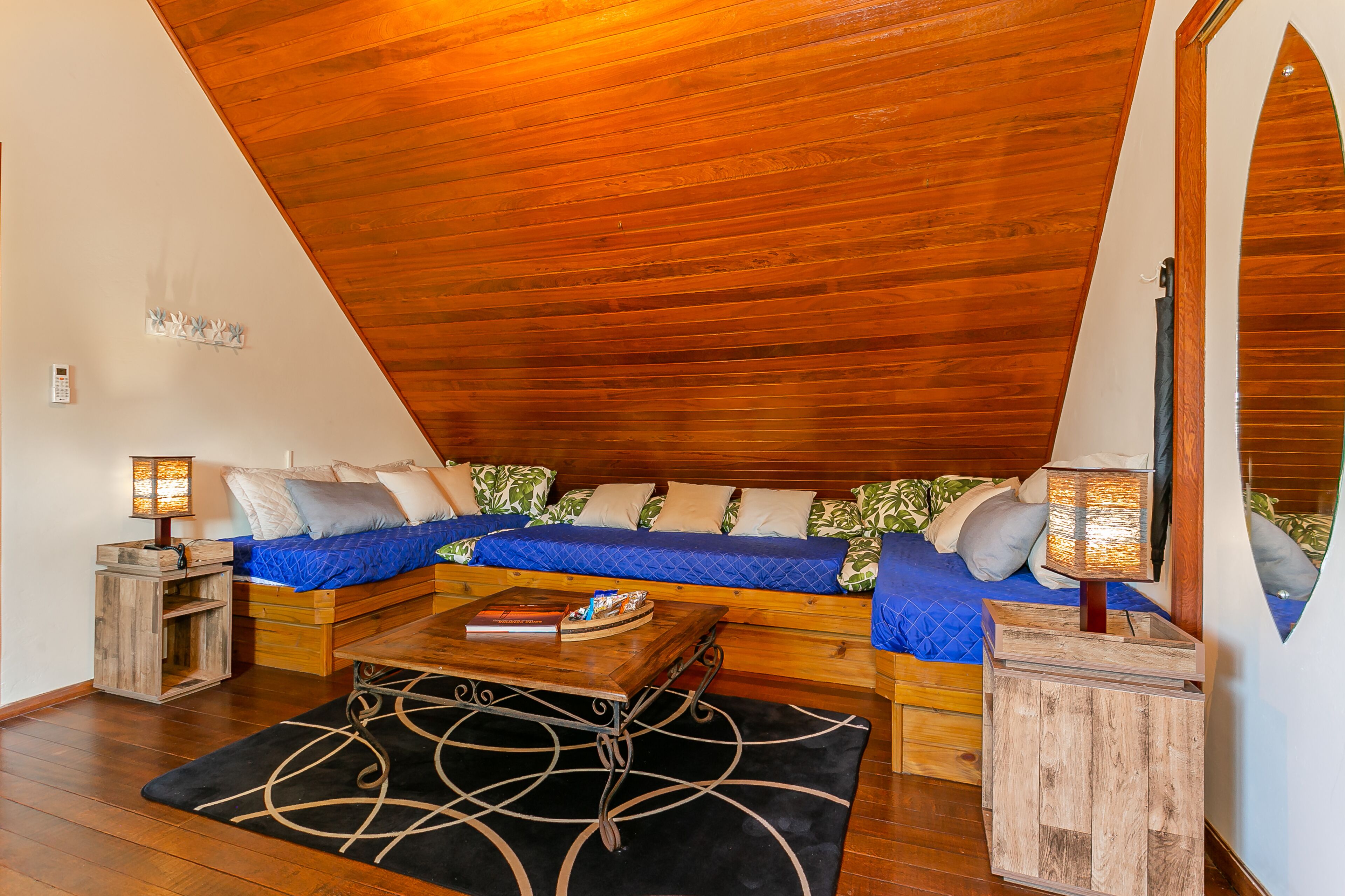 Une chambre à coucher confortable, aménagée en mezzanine, avec un plafond en pente, un lit en bois avec une literie bleue, une petite table en bois et une table de chevet avec une lampe.