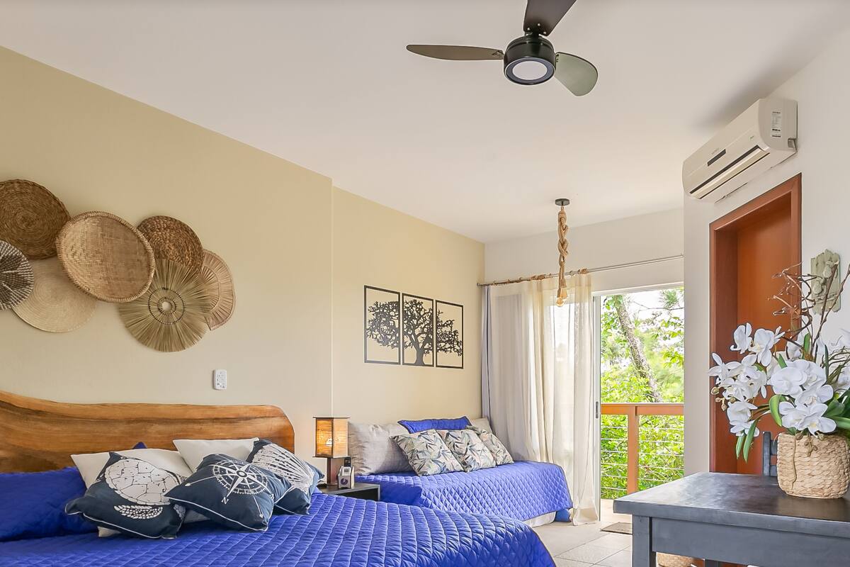 A bedroom with two beds, a ceiling fan, and a view of greenery outside.
