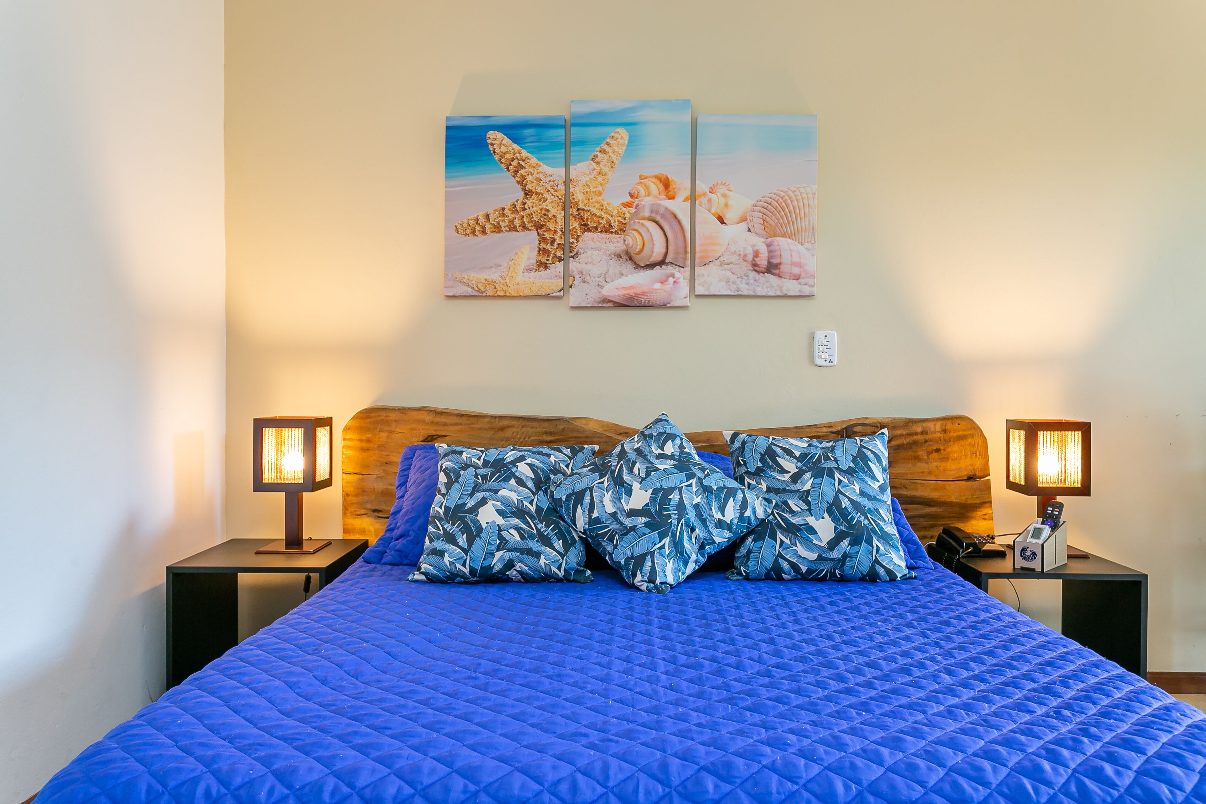 A bed with a blue quilt, wooden headboard, and two nightstands with lamps.