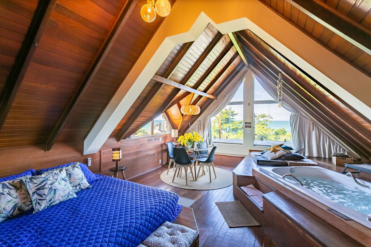 A spacious attic bedroom with a large bed, a sitting area, and a hot tub.