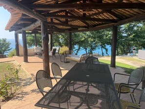 An outdoor patio with a covered area, seating, and a view of the sea.