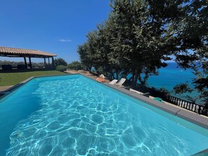 A clear blue swimming pool with lounge chairs and a view of the sea.