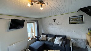 Ein gemütliches Wohnzimmer mit einem dunkelblauen Sofa, einem wandmontierten Flachbildfernseher und einer Deckenleuchte.