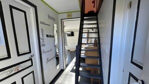 Ein Flur mit einer Treppe, einer Tür mit Schwarz-Weiß-Muster sowie einer Wand mit den Schildern 'Welcome' und 'Bienvenue'.