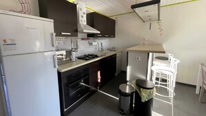 Eine moderne Küche mit Kühlschrank, Herd, Backofen und Spüle. Zwei Mülleimer und eine kleine Bar mit Hockern sind vorhanden.