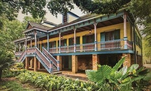 Un edificio de estilo colonial de dos pisos con un balcón y una escalera que conduce al nivel superior.