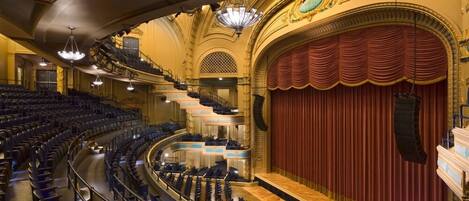 Een theater met een groot podium, meerdere balkons en versierde architectuur.
