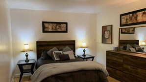 Ein Schlafzimmer mit einem hölzernen Bett, zwei Nachttischen mit Lampen, einer Kommode und gerahmten Kunstwerken an den Wänden.