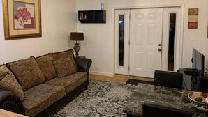 Ein Wohnzimmer mit einer Couch, einem Couchtisch, einer Lampe, einem Fernseher und einer Tür zu einem anderen Raum.