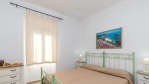 Une chambre à coucher avec un lit, une table de chevet, une commode, une fenêtre avec des rideaux et un tableau au mur.