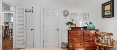 A bedroom with a wooden dresser, two beds, a ceiling fan, and a door leading to another room.