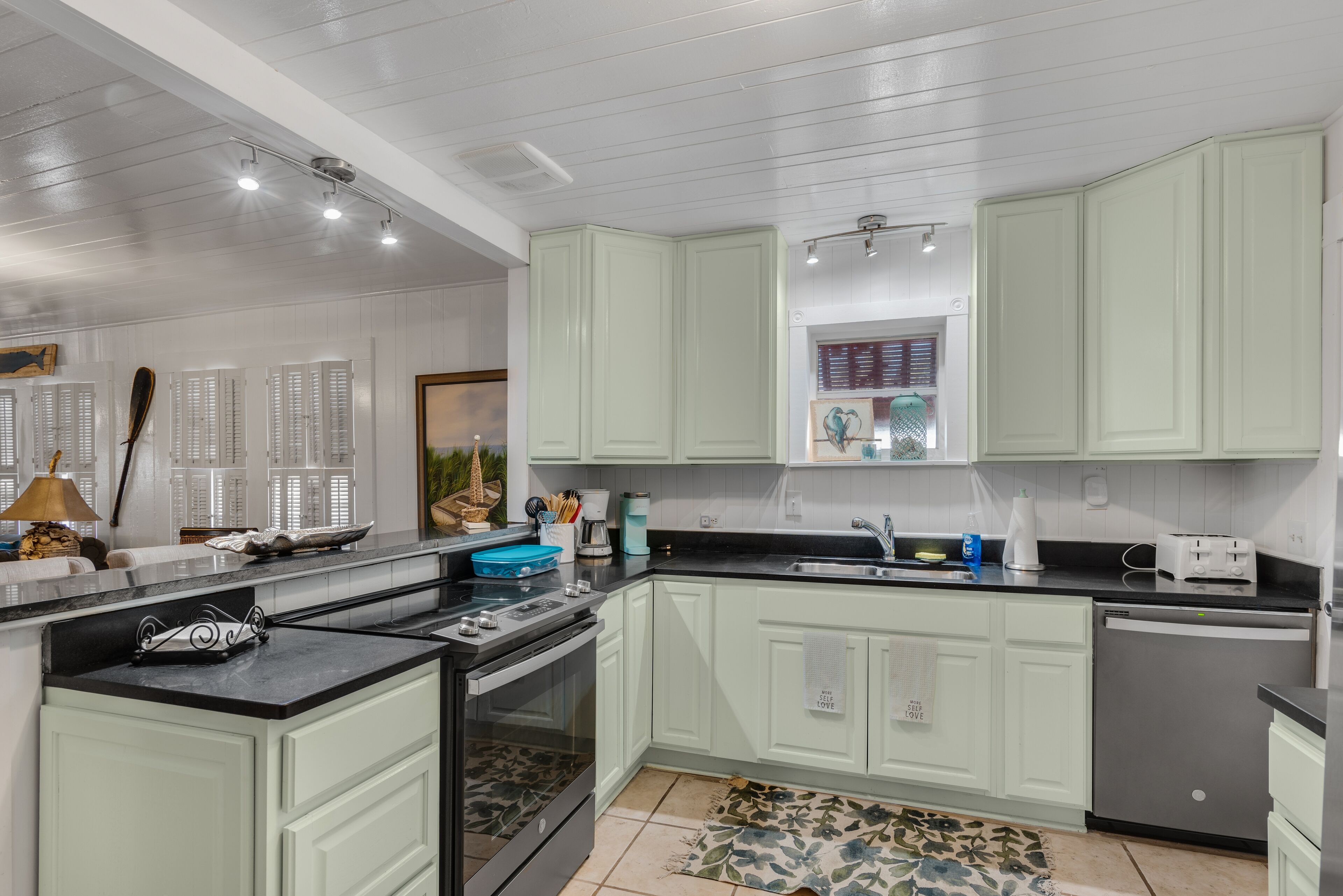 A kitchen with light green cabinets, a black countertop, and a dishwasher.