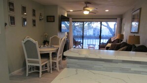 A modern kitchen with a marble countertop, dining area with chairs, and a view through large windows. - Lakeside Daze! (Montgomery)