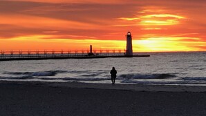 A beach with a lighthouse and a pier extending into the sea during sunset. - Cozy Efficiency at Downtown Manistee (Manistee)
