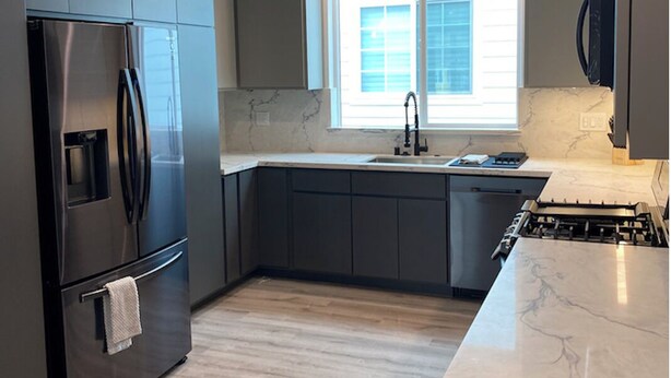 Una cocina moderna con armarios oscuros, un refrigerador de acero inoxidable, encimera de mármol y una ventana que deja entrar luz natural.