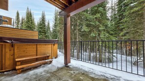 A wooden deck with a bench, a metal railing, and a snowy forest backdrop.