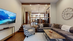 A modern living room with a large flat-screen TV, a sofa, a coffee table, and a patterned armchair.