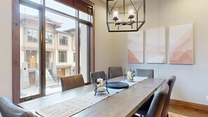 A dining area with a long table, chairs, a chandelier, and artwork on the wall.