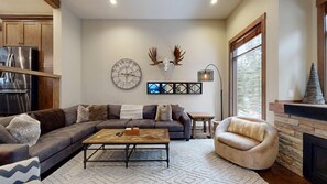 A modern living room with a sectional sofa, a coffee table, a fireplace, and a large window.