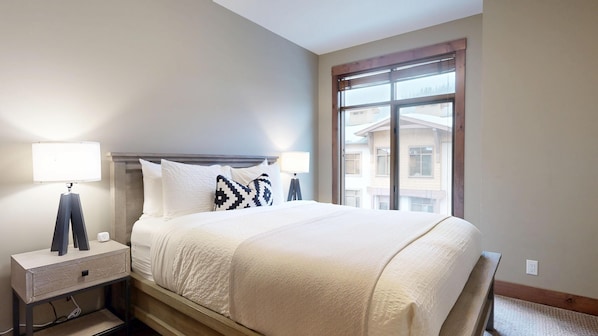 A hotel room with a bed, bedside lamps, a nightstand, and a window with a view of buildings.